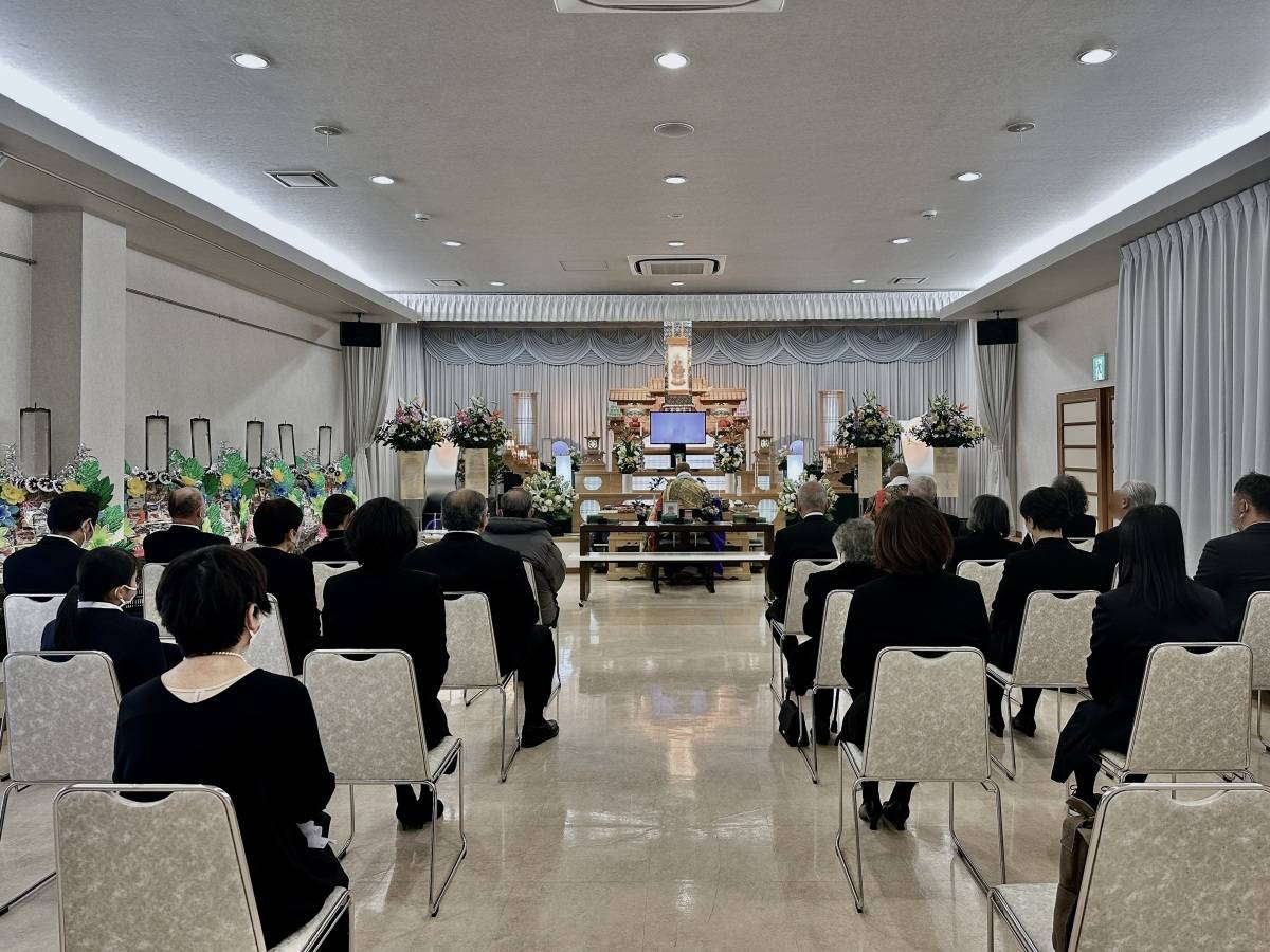 葬儀会場で、祭壇に向かって椅子に座る参列者たちの後ろ姿。