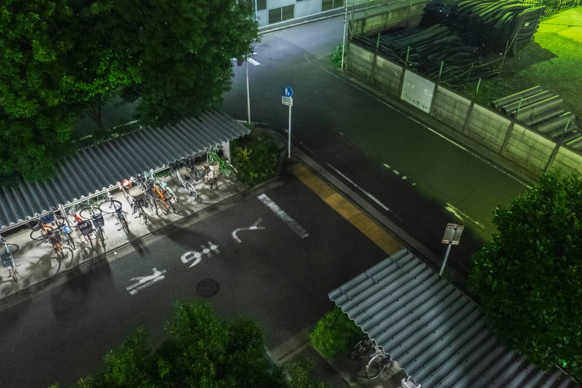 夜の屋外駐輪場を上から見下ろした風景。屋根の下に複数の自転車が並んでいる。