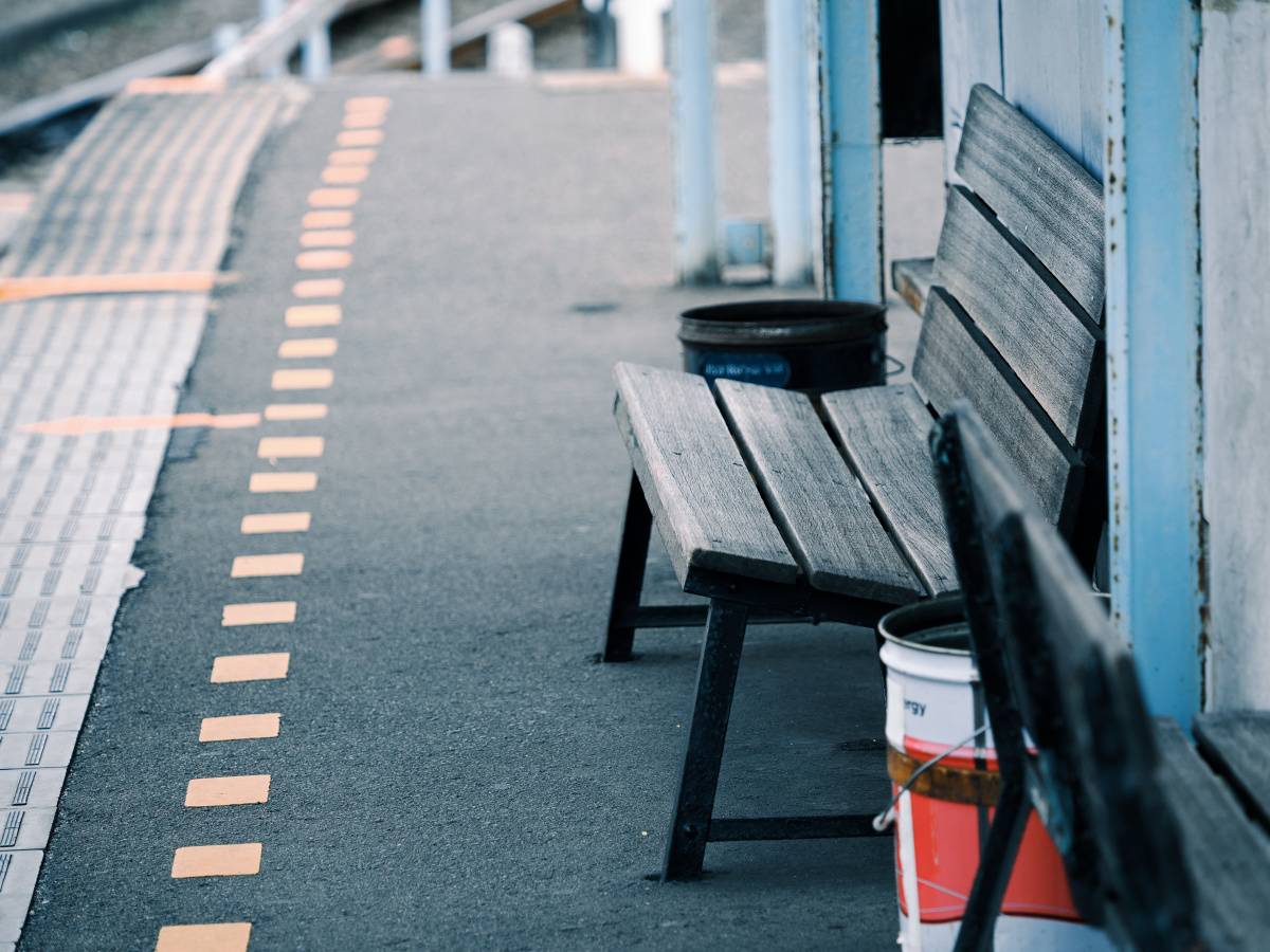 駅のホームに設置された古い木製ベンチ。奥には線路沿いに続くホームが見える。