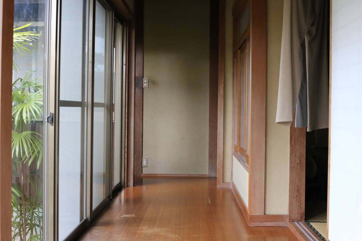 木製の床が続く日本家屋の廊下。左側には庭に面したガラス戸が並び、右側には和室の入り口が見える。