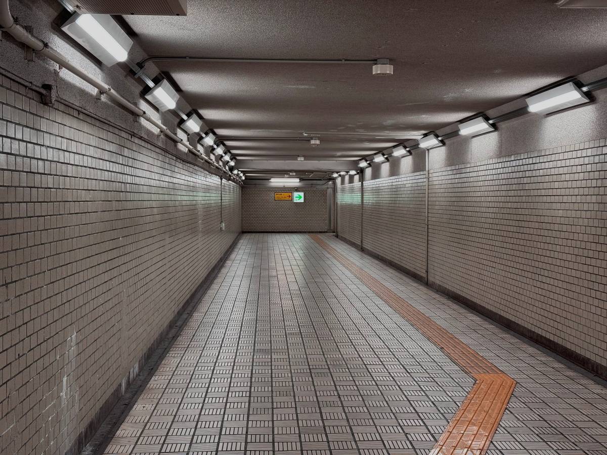 白いタイル張りの壁と床が続く地下通路。天井には照明が並び、床には点字ブロックが敷かれている。
