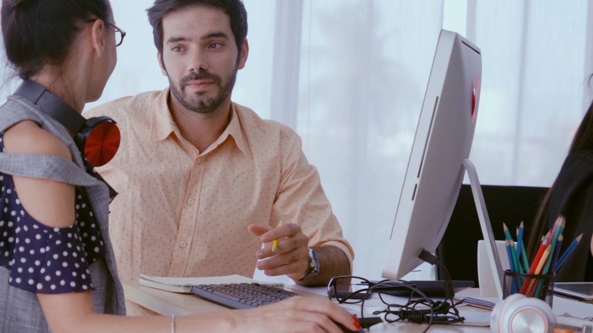 デスクで同僚と話す男性