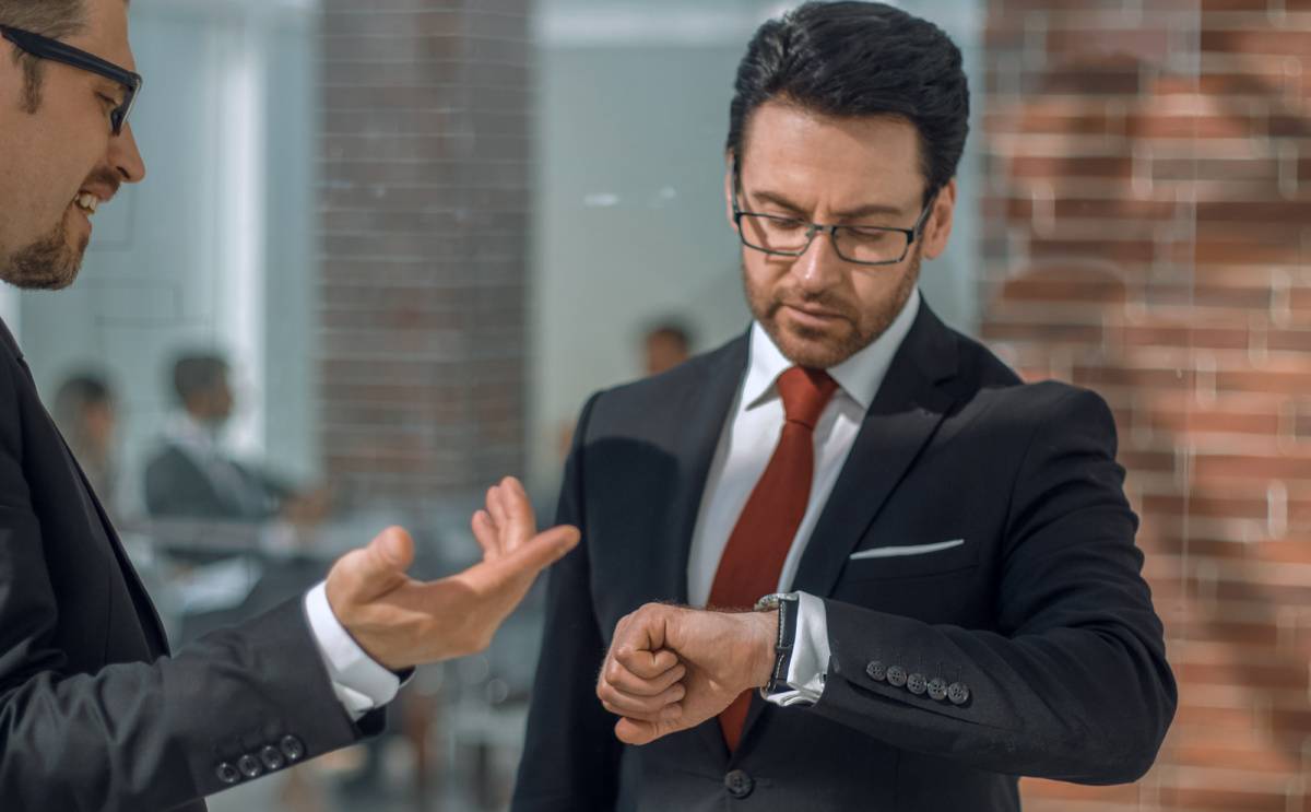 同僚と話しながら時間を気にする男性