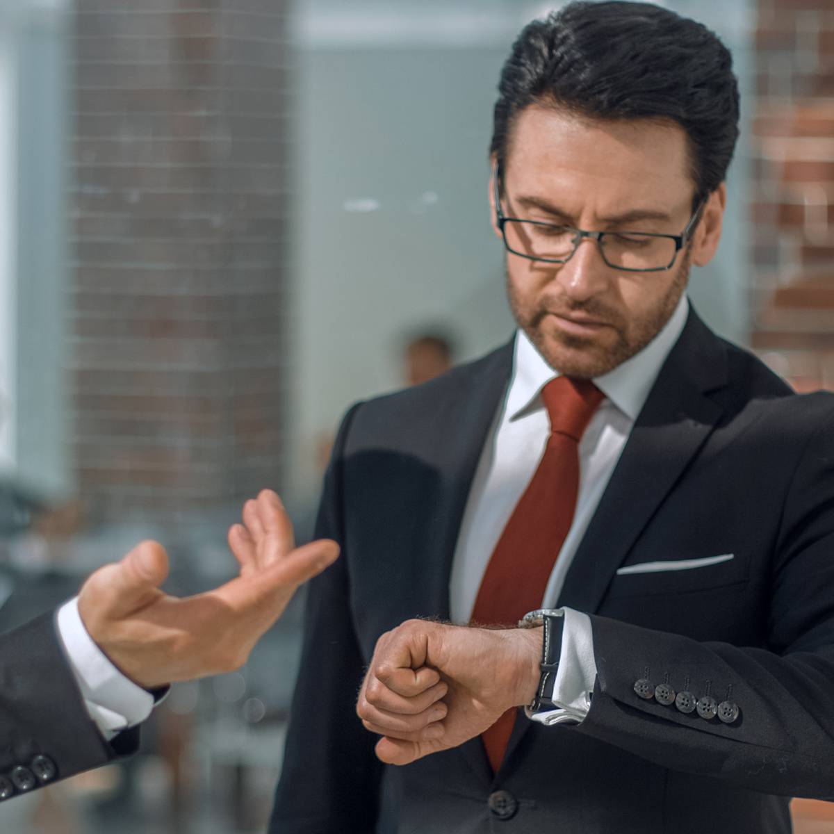 同僚と話しながら時間を気にする男性