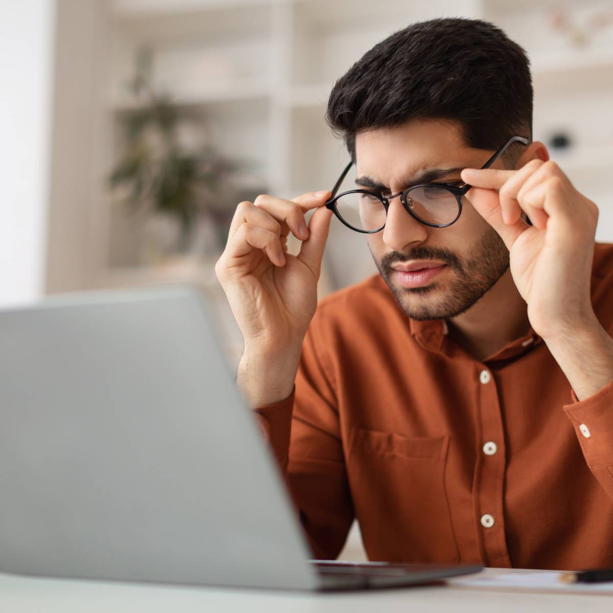 眼鏡に手を添えてパソコンを見つめる男性