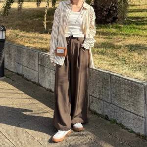  ストライプ柄のシャツにブラウンパンツを合わせた女性 