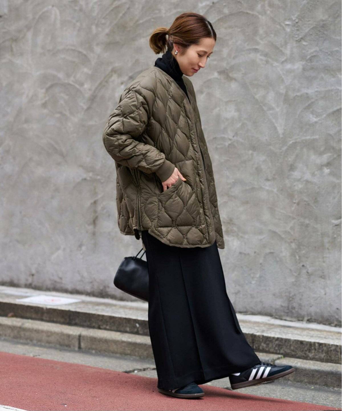 カーキのキルティングコートにスカートを合わせた女性