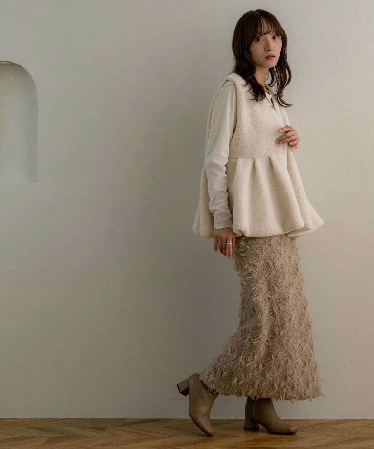 白トップスにベージュのベストを重ねて白パンツを穿いた女性