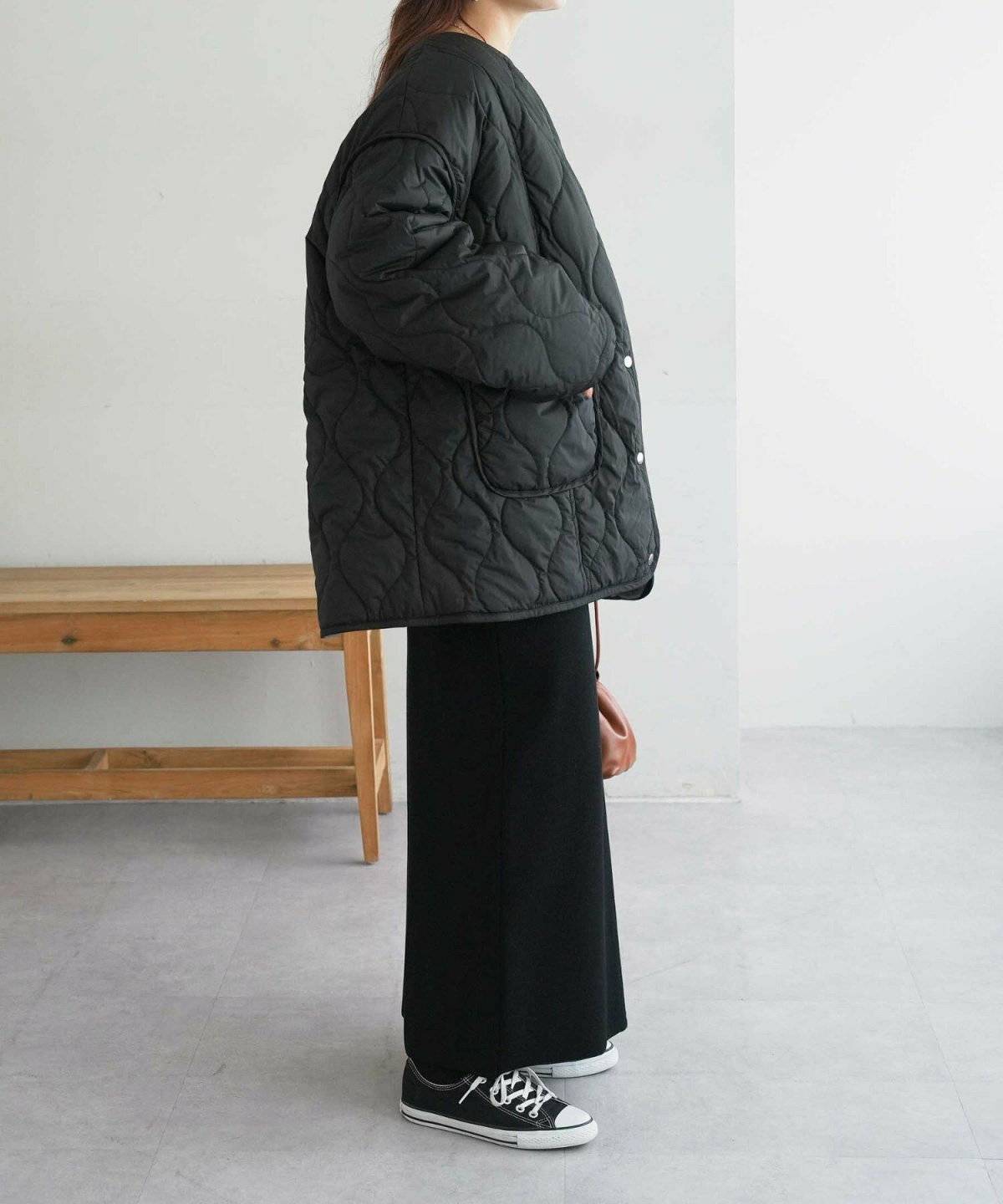 グリーンのキルティングコートに黒パンツを合わせた女性