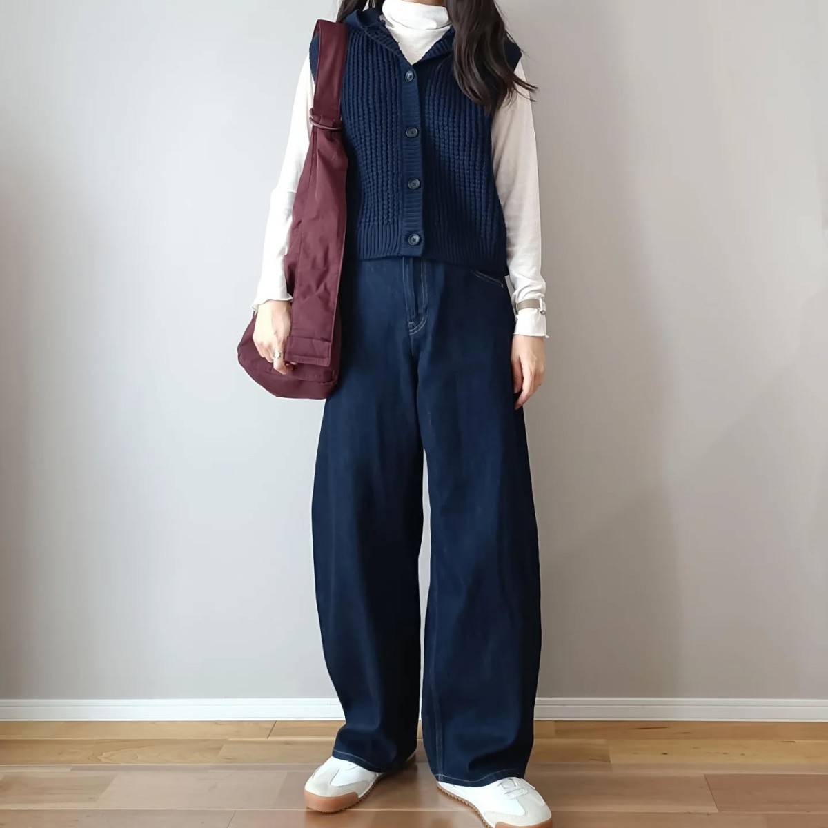 白トップスにネイビーのベストを重ね着してデニムパンツを穿いた女性