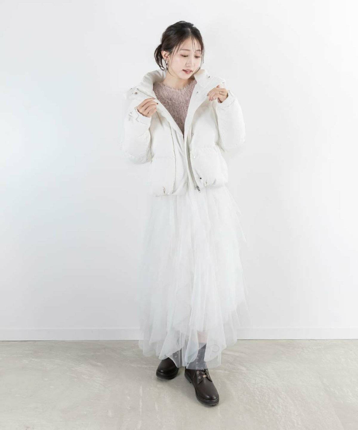 グレーのニットに白スカートを合わせて白ダウンを羽織った女性