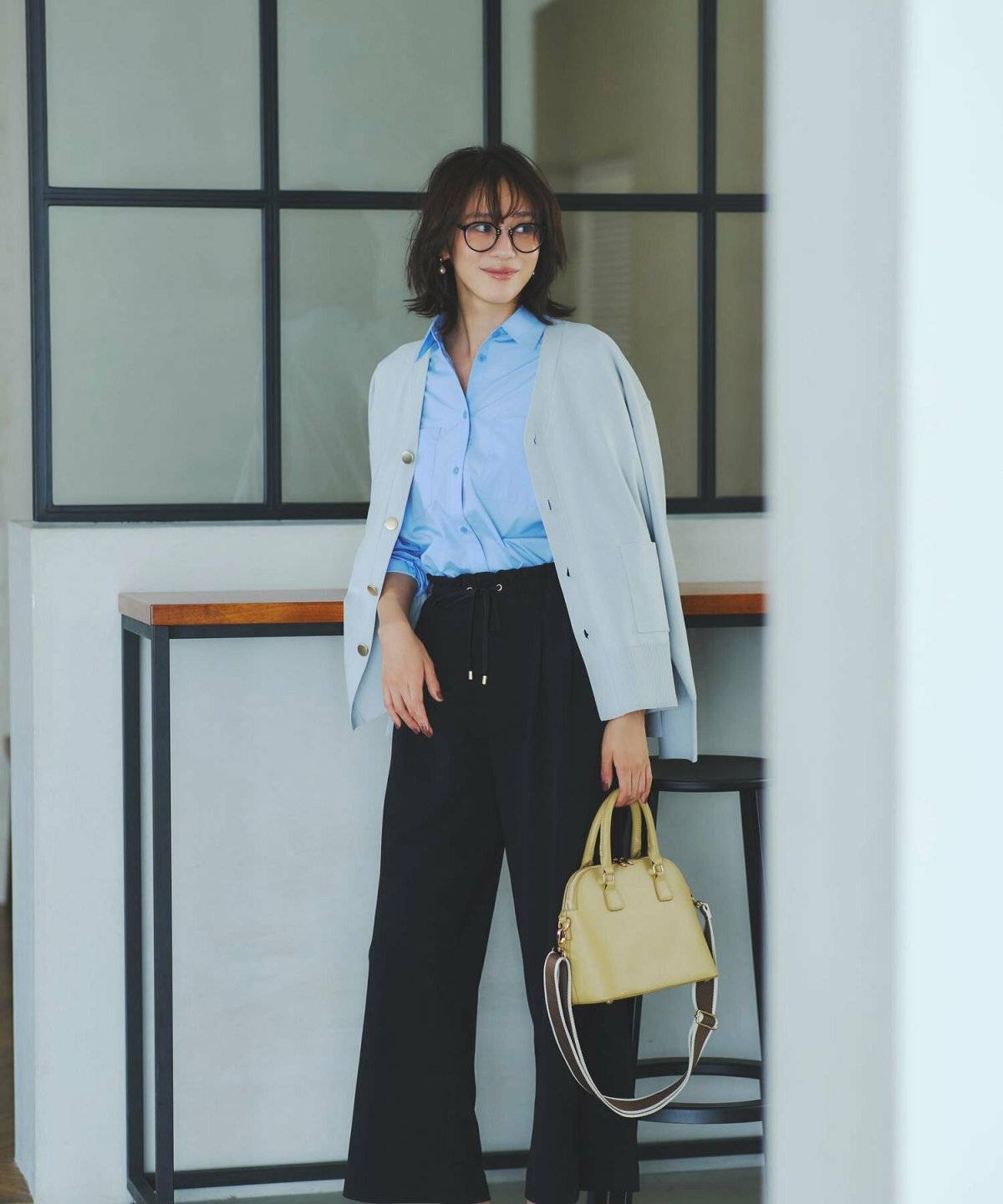 シャツにグレーのカーディガンを合わせて黒パンツを穿いた女性