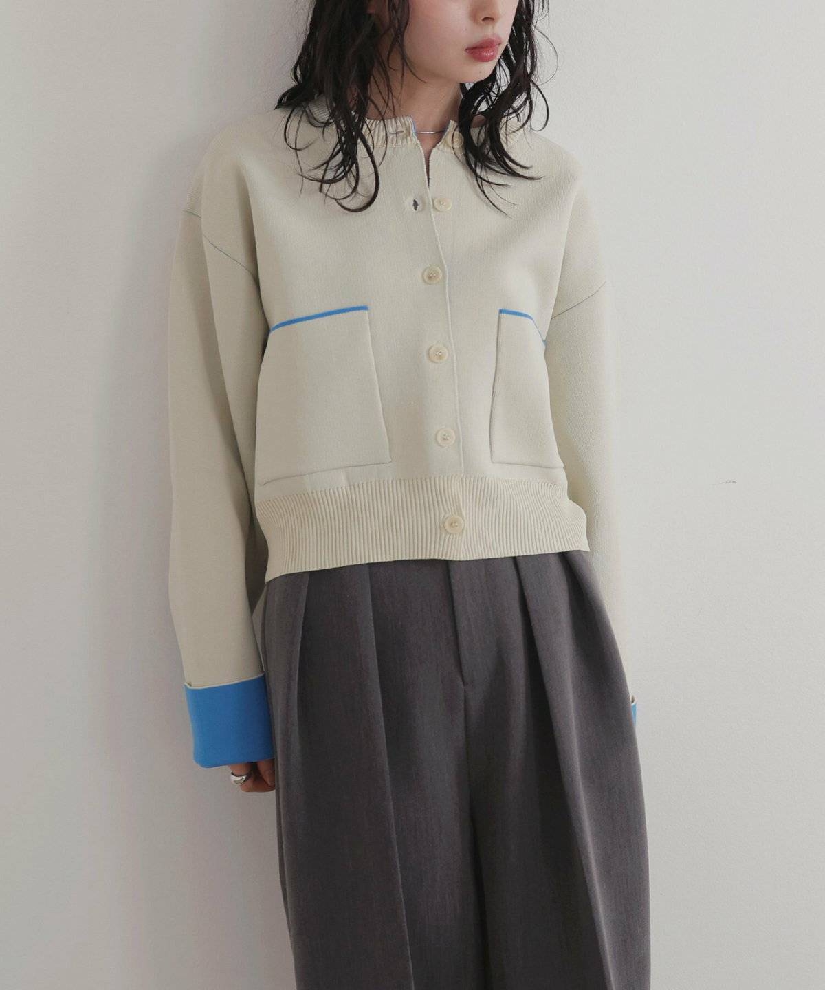 白ニットカーディガンにグレーのパンツを合わせた女性