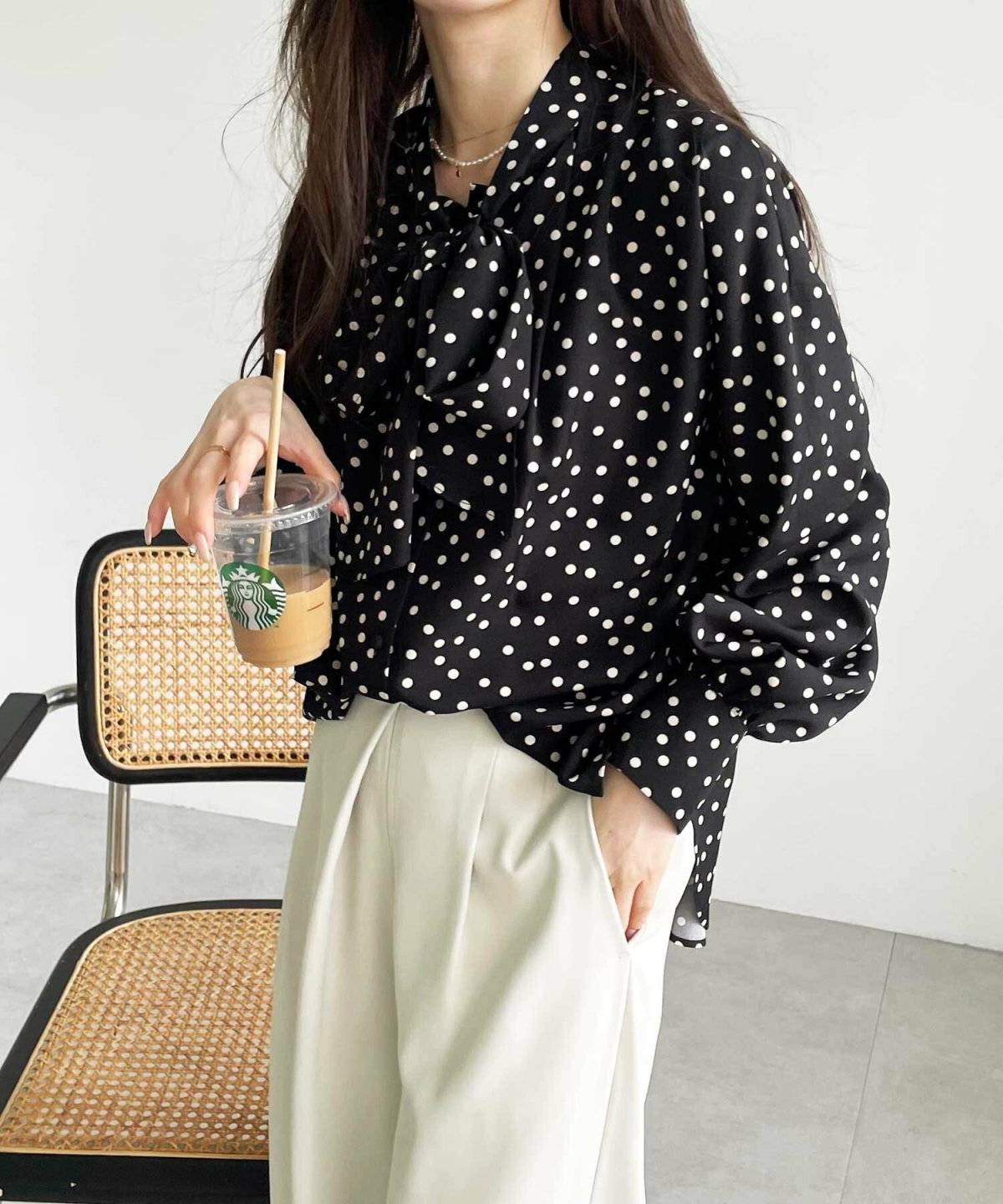 黒のドット柄ブラウスにベージュのパンツを合わせた女性