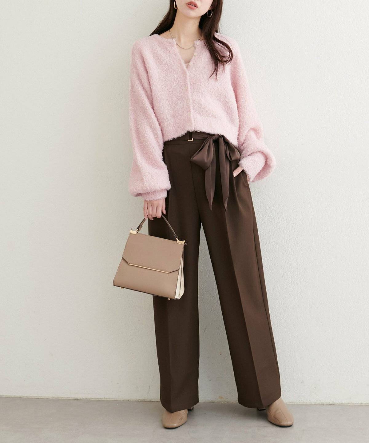 ピンクのカーディガンにブラウンのパンツを合わせた女性
