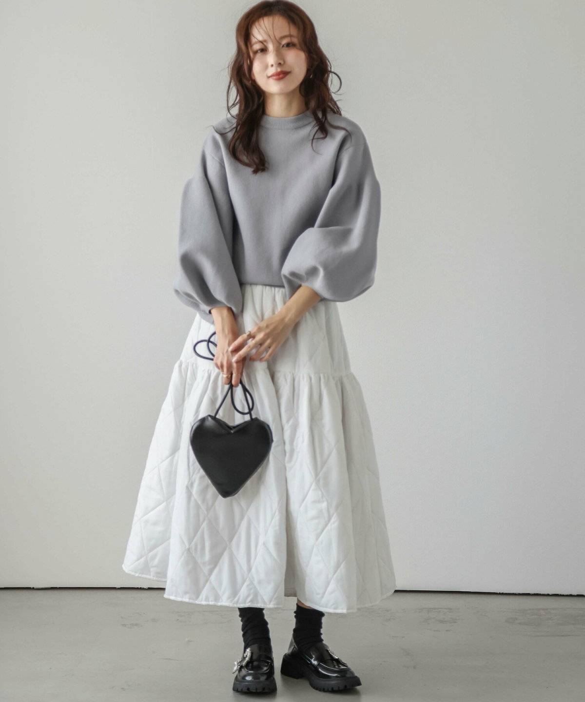 グレーのハイネックニットに白スカートを合わせた女性