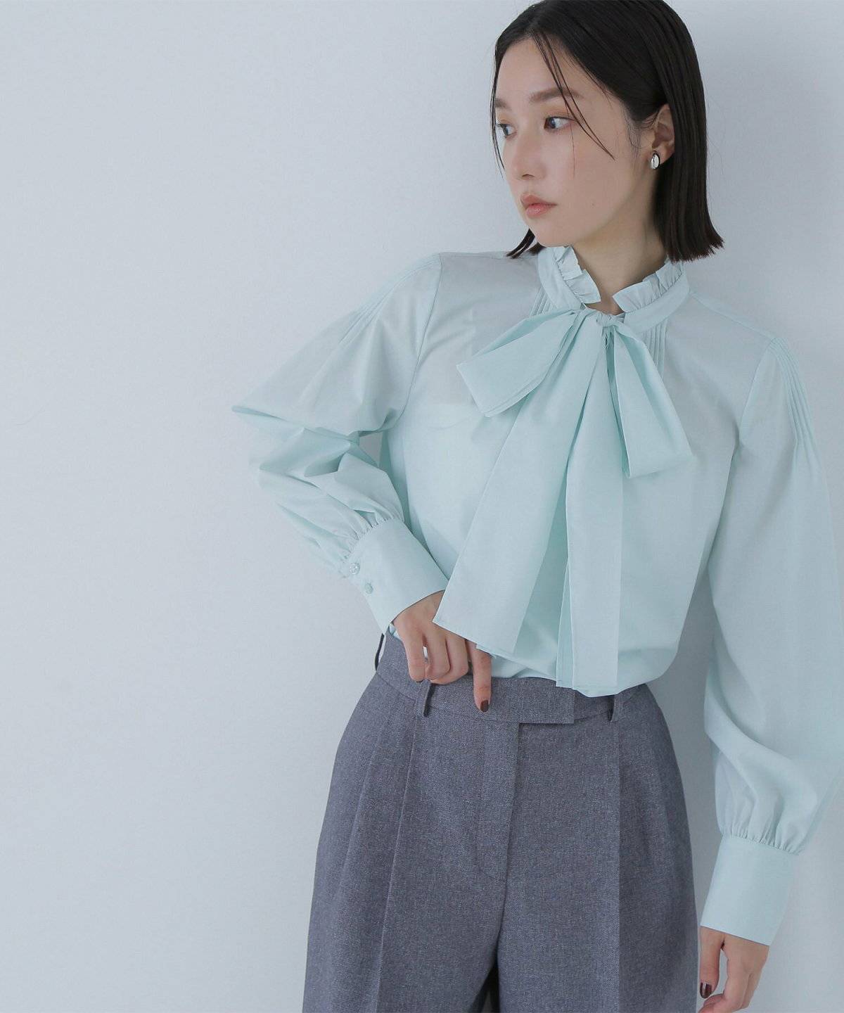 グリーンのブラウスにパンツを合わせた女性