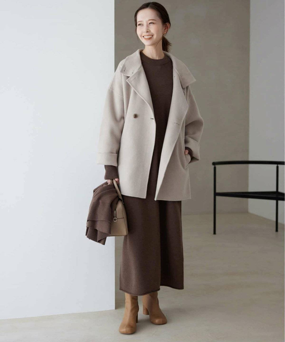 ブラウンのニットワンピースにベージュのコートを羽織った女性