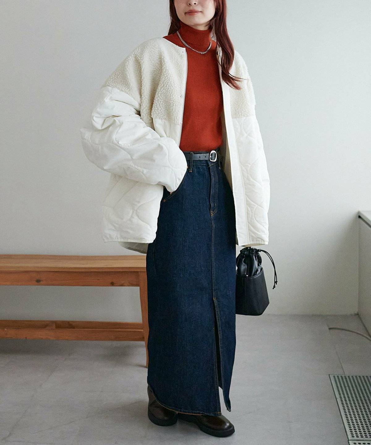 ハイネックトップスにデニムワンピースを重ねてキルティングコートを羽織った女性
