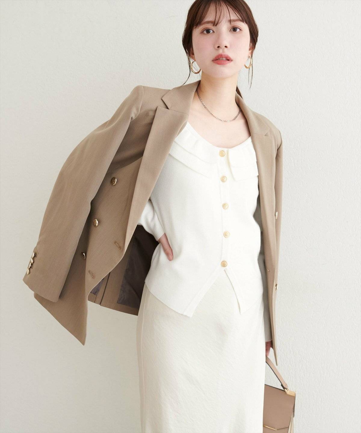 ホワイトコーデにベージュのジャケットを羽織った女性