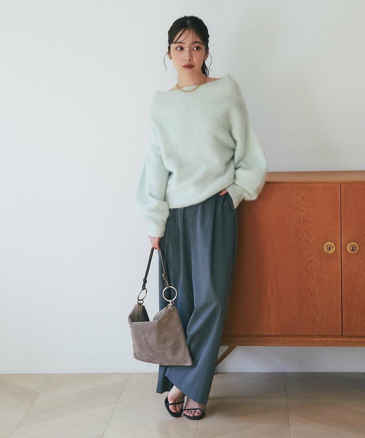 グリーンのニットにグレーのパンツを合わせた女性