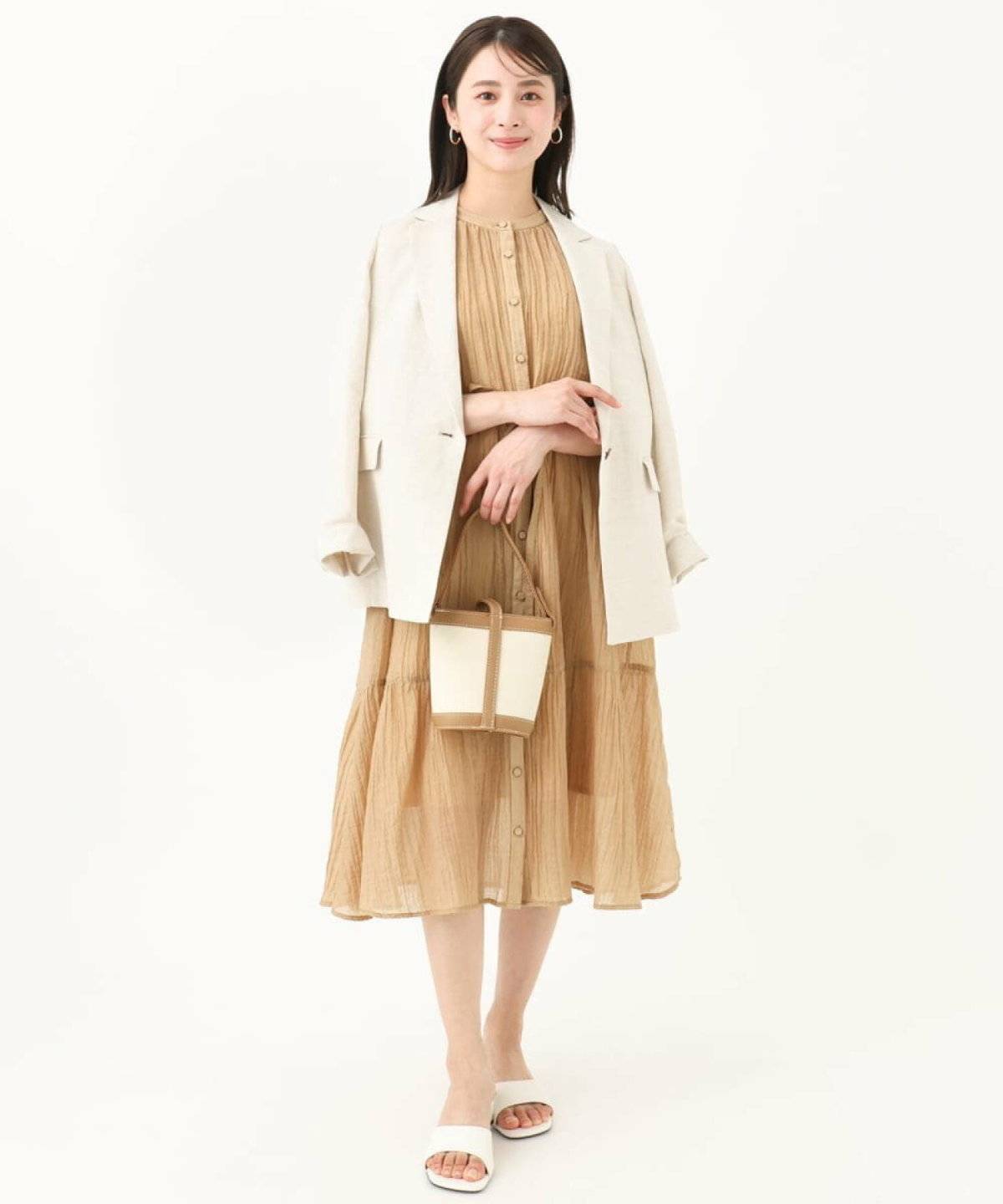 ベージュのワンピースにジャケットを羽織った女性