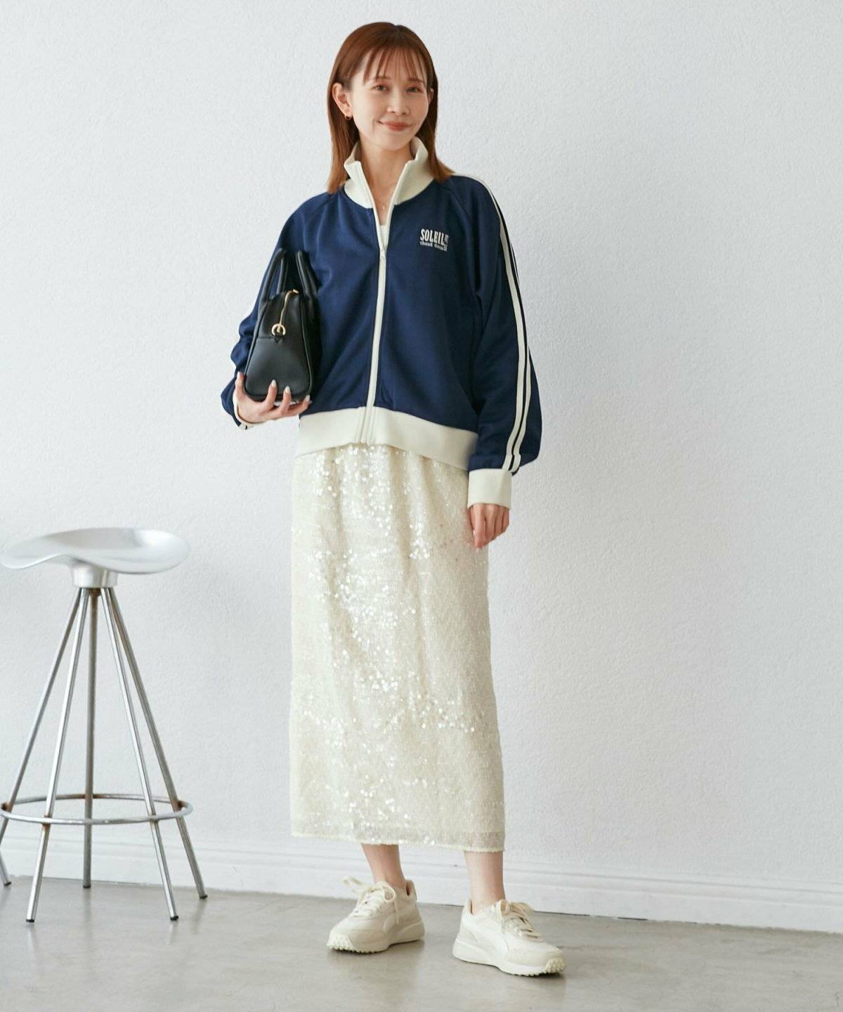 ネイビーのトラックジャケットに白スカートを合わせた女性
