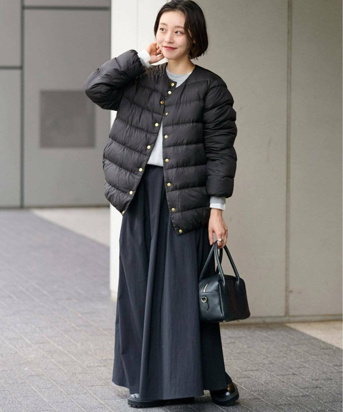 グレーのニットに黒スカートを合わせて黒ダウンを羽織った女性