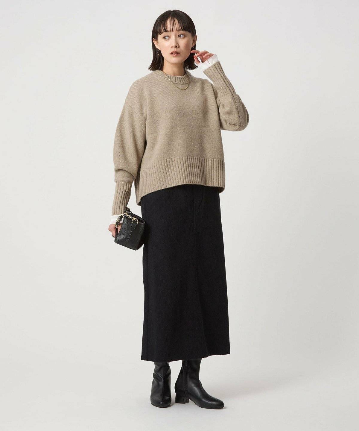 ベージュのニットに黒スカートを合わせた女性