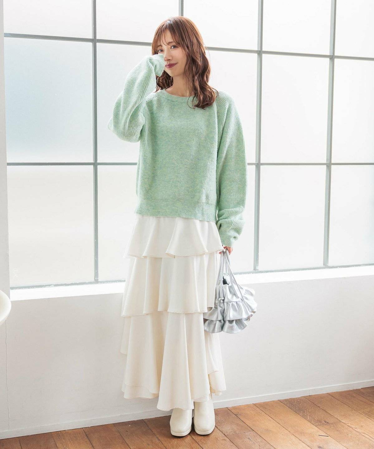 グリーンのニットに白スカートを合わせた女性