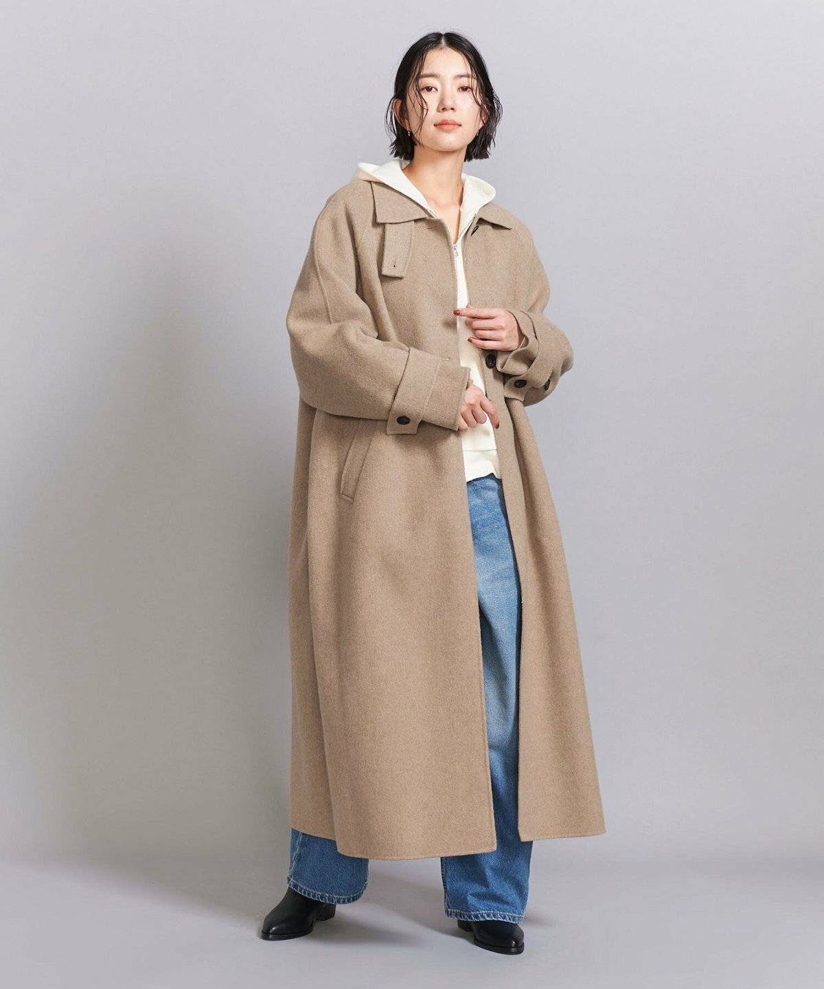 パーカーとデニムにベージュコートを羽織った女性