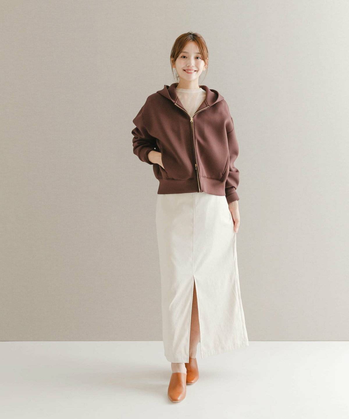 ブラウンのパーカーに白スカートを合わせた女性