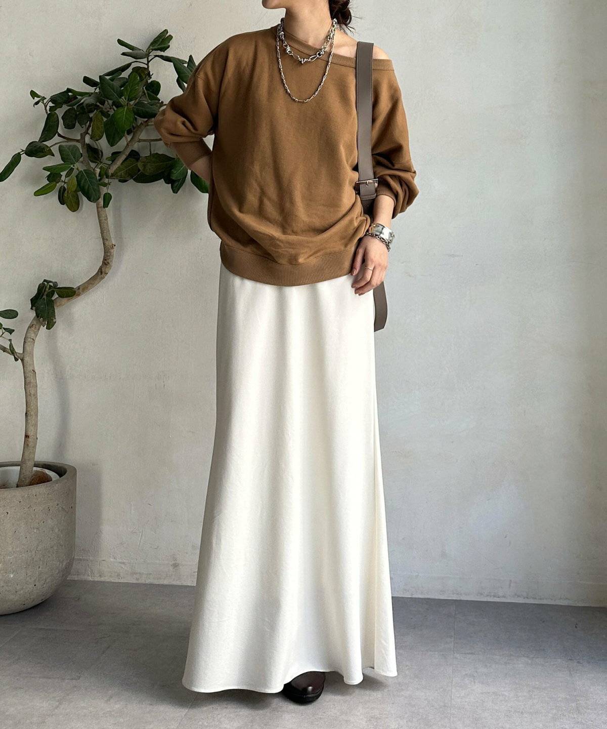 ブラウンのスウェットに白スカートを合わせた女性