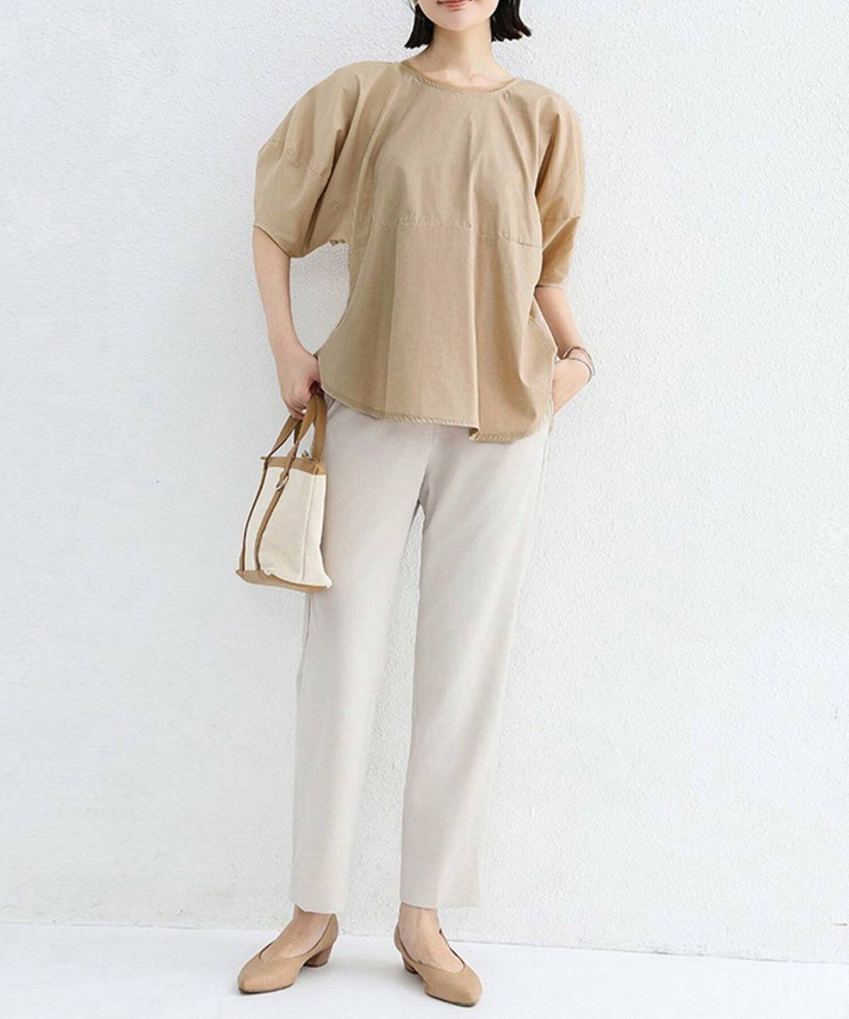 ベージュのブラウスにホワイトのパンツを合わせた女性