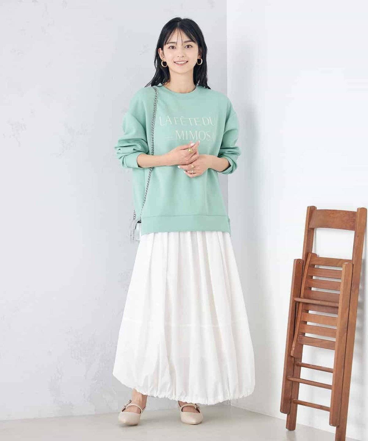グリーンスウェットに白スカートを合わせた女性