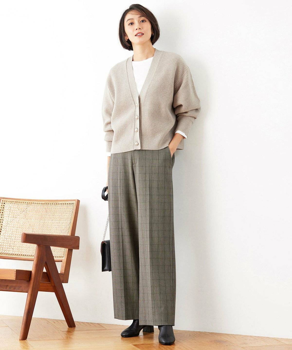 ベージュのカーディガンにチェック柄パンツを合わせた女性