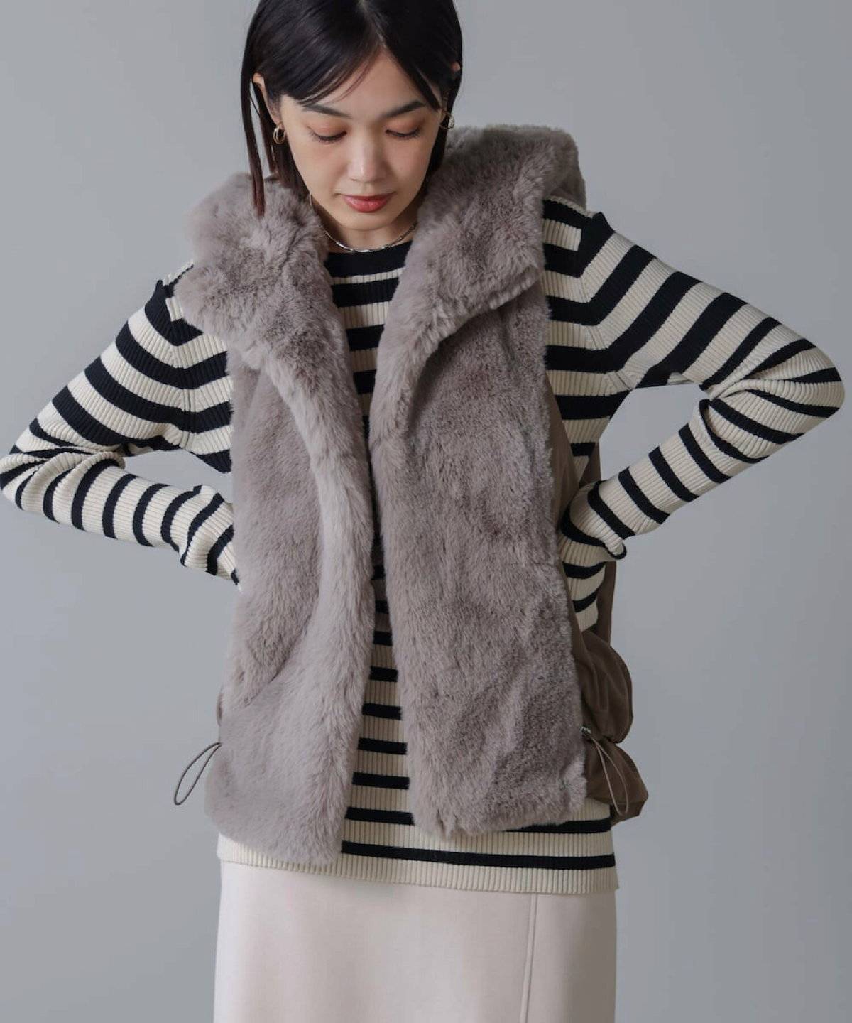 ボーダー柄ニットにファーベストを重ねてニットスカートを合わせた女性