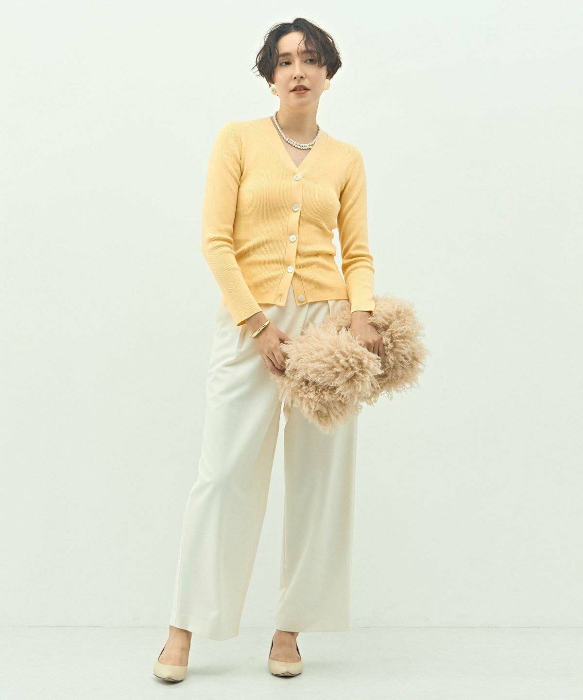 イエローのカーディガンに白パンツを合わせた女性