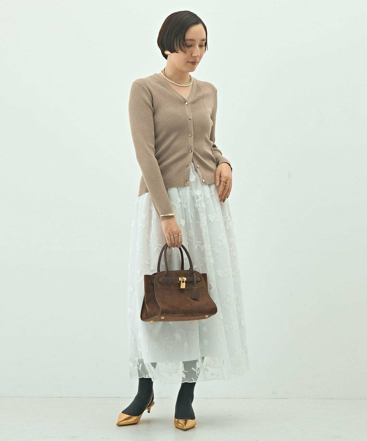 キャメルのカーディガンに白スカートを合わせた女性