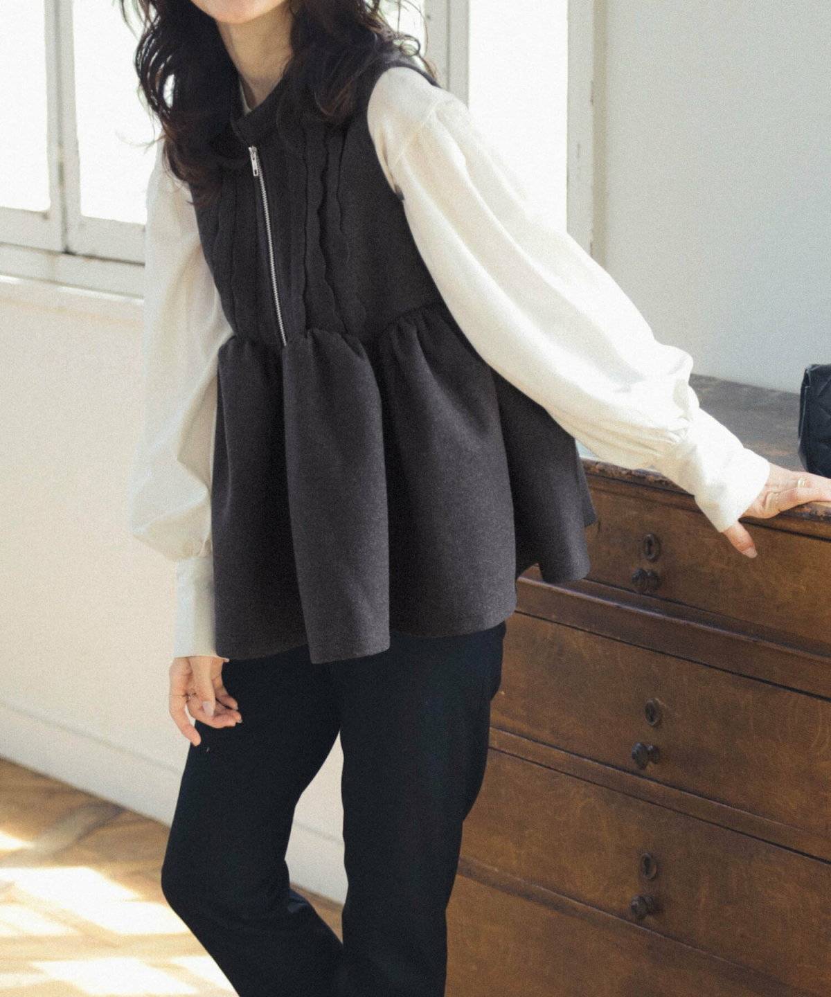 白ブラウスにベストを重ねてデニムを穿いた女性