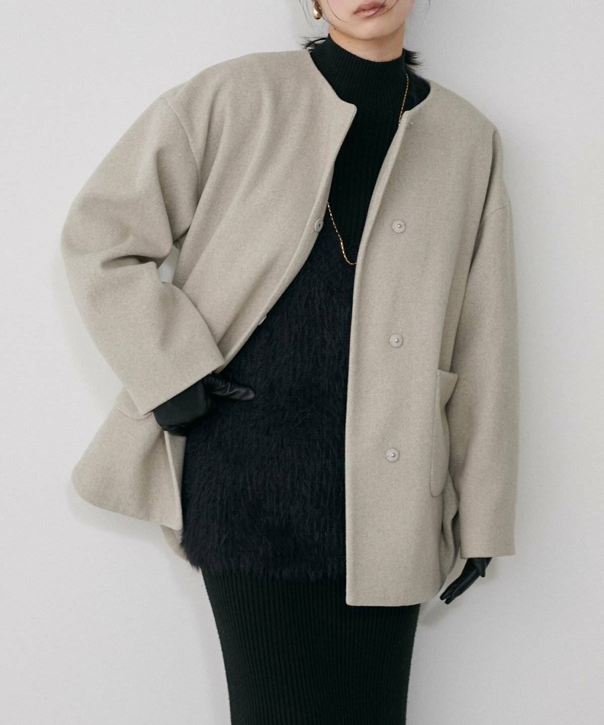 ブラックコーデにベージュのニットコートを羽織った女性