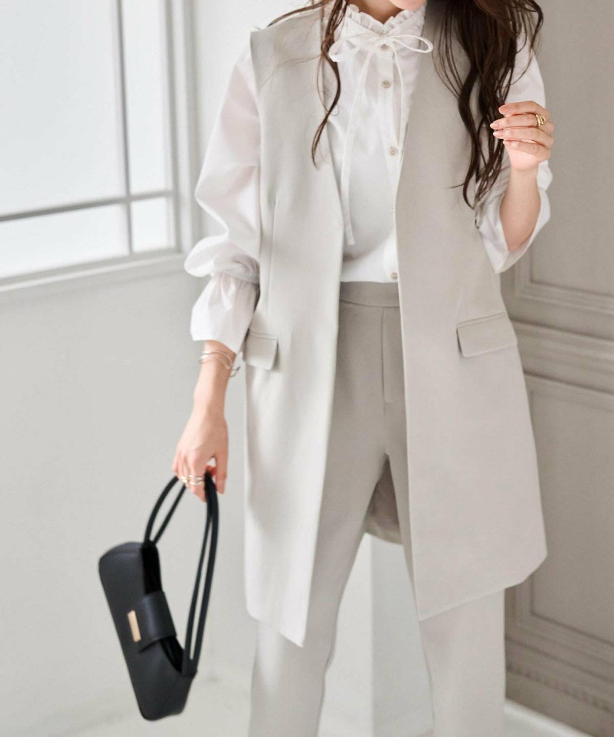 白シャツにベージュのベストを重ねてベージュのパンツを穿いた女性