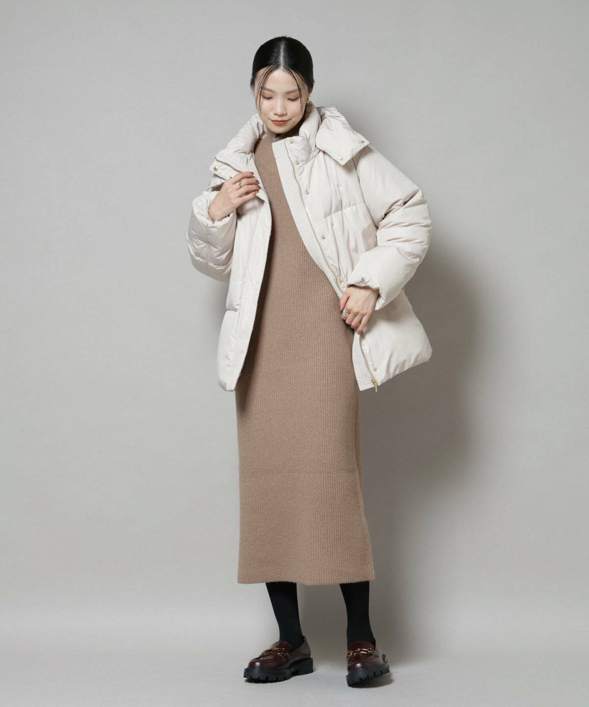 ブラウンのニットワンピースに白ダウンを羽織った女性
