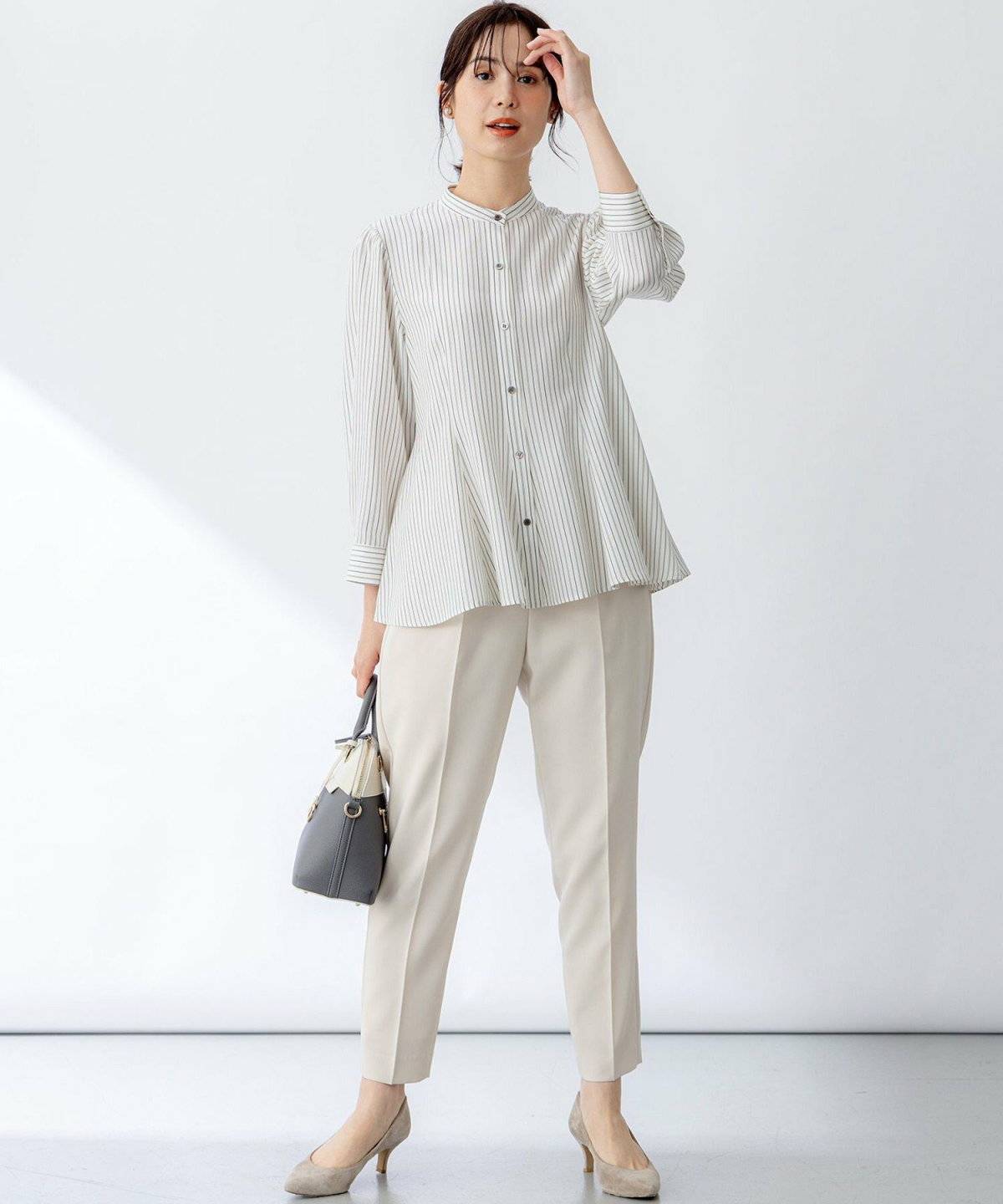 ベージュのストライプ柄ブラウスに白パンツを合わせた女性