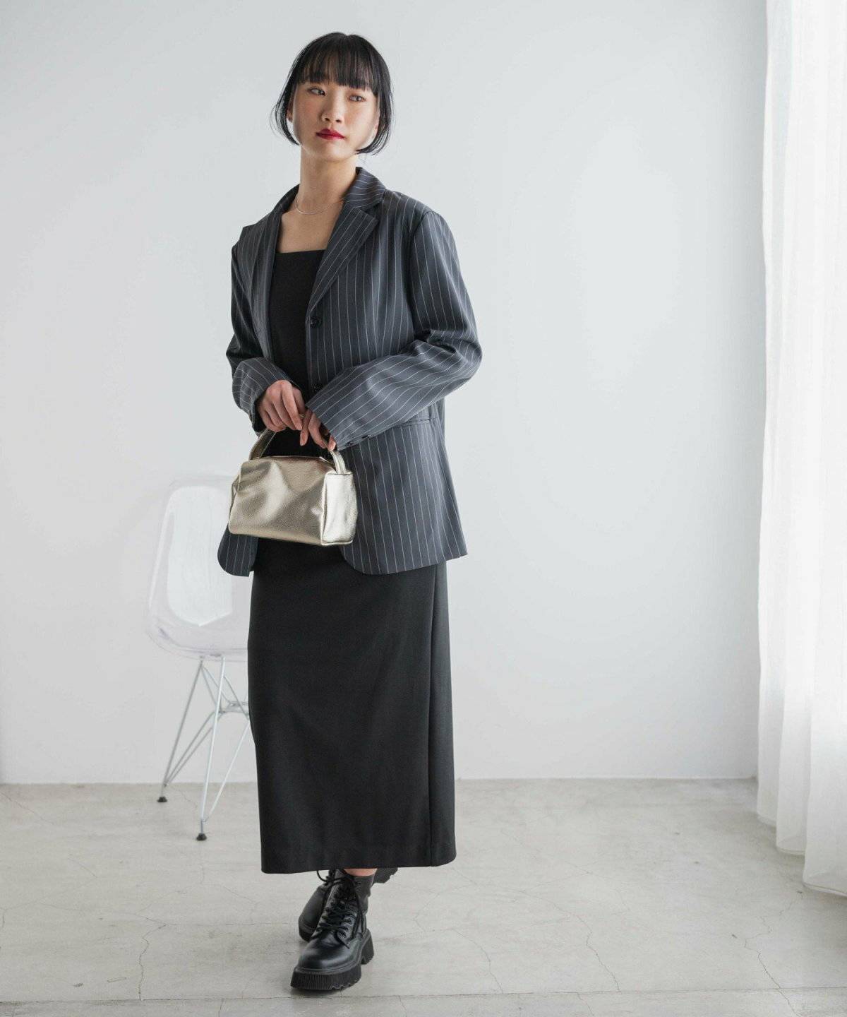 黒ワンピースにストライプ柄ジャケットを羽織った女性