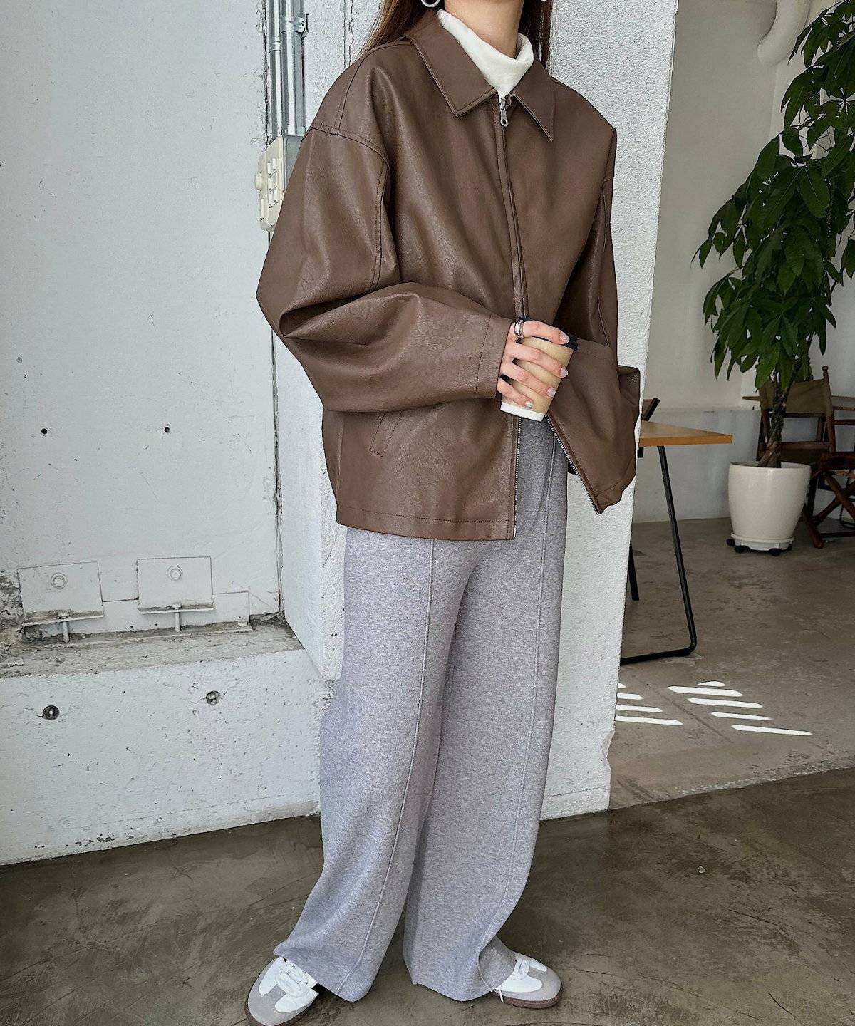 ブラウンのフェイクレザーブルゾンにグレーのパンツを合わせた女性