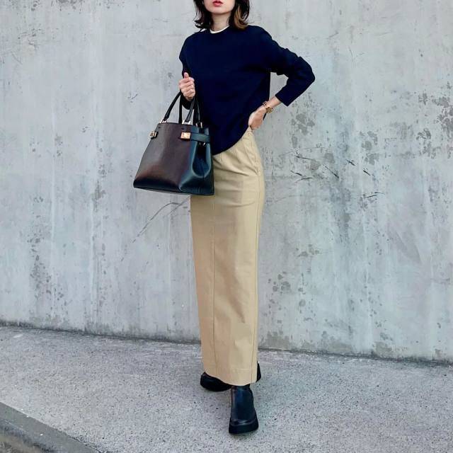 ネイビーのニットにベージュのスカートを合わせた女性