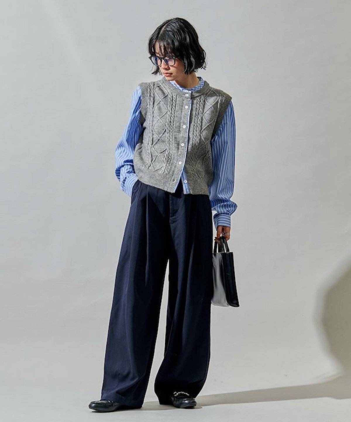 ストライプ柄シャツにニットベストを重ねてパンツを合わせた女性