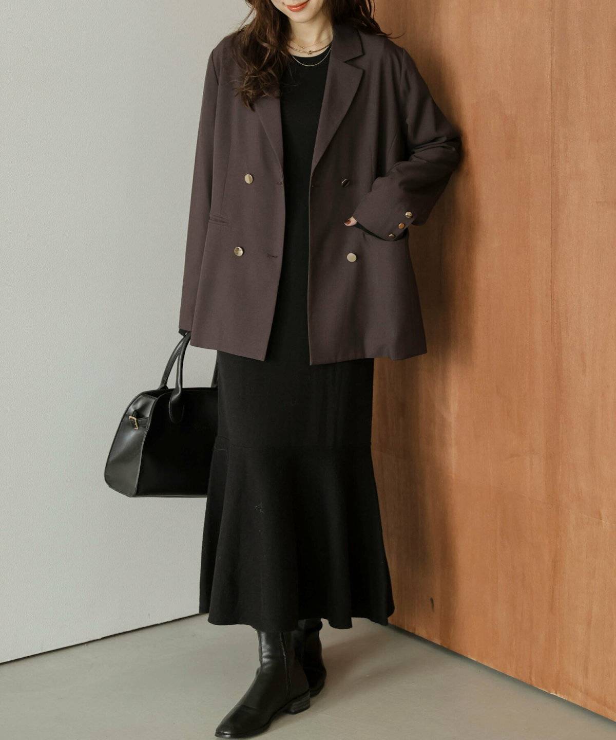 黒ワンピースにブラウンのジャケットを羽織った女性