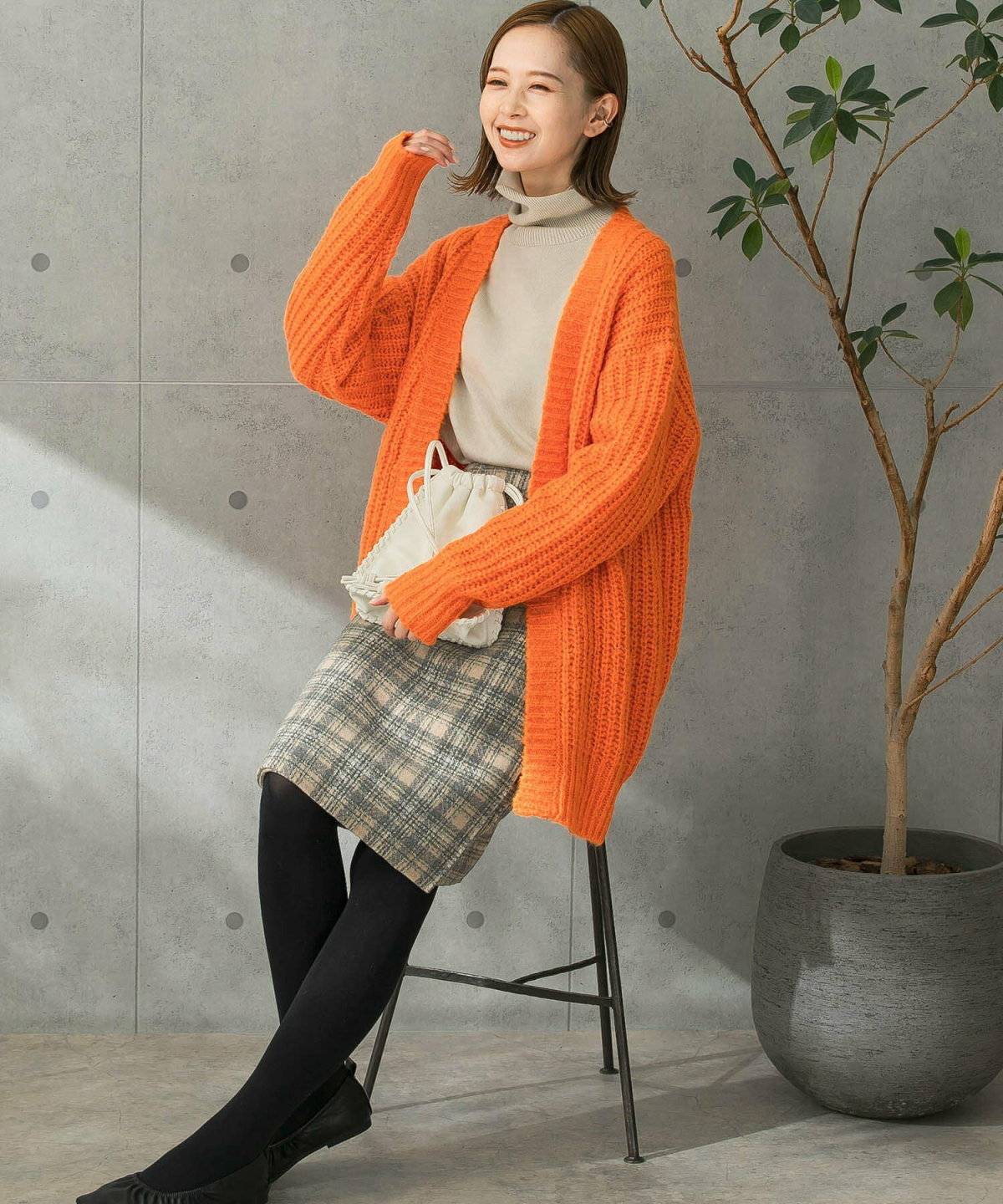 オレンジカーディガンにチェック柄スカートを合わせた女性